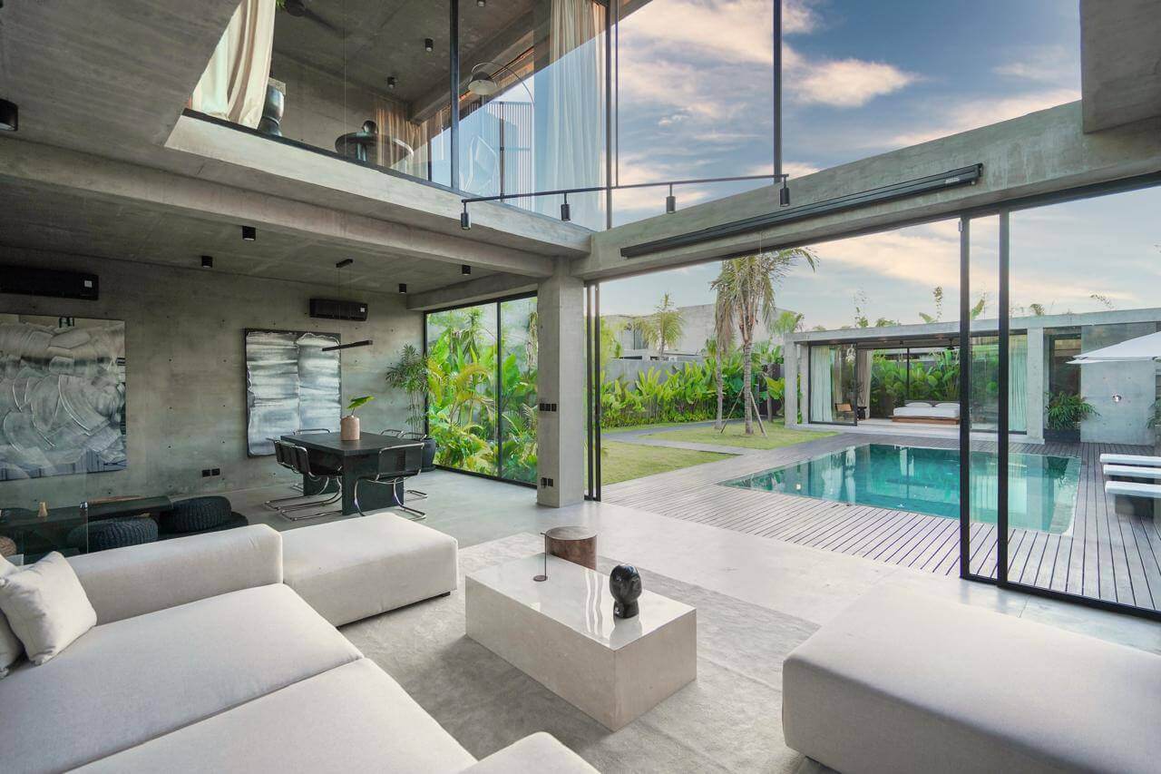 Concrete loft-style villa living room opening onto pool and garden — Frigate Bali