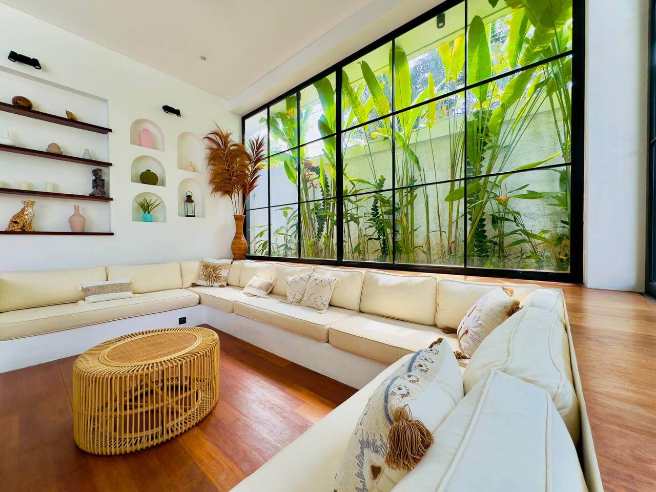 Bright villa lounge with beige corner sofa and indoor garden window — Frigate Bali